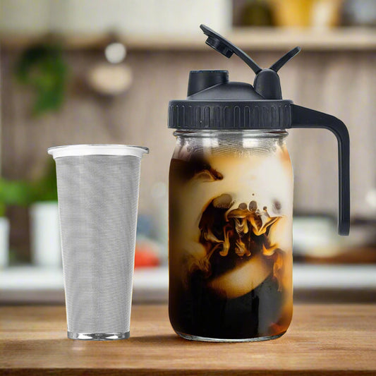 Mason jar with black lid and straw, filled with iced coffee, next to a clear shaker cup on a white background.