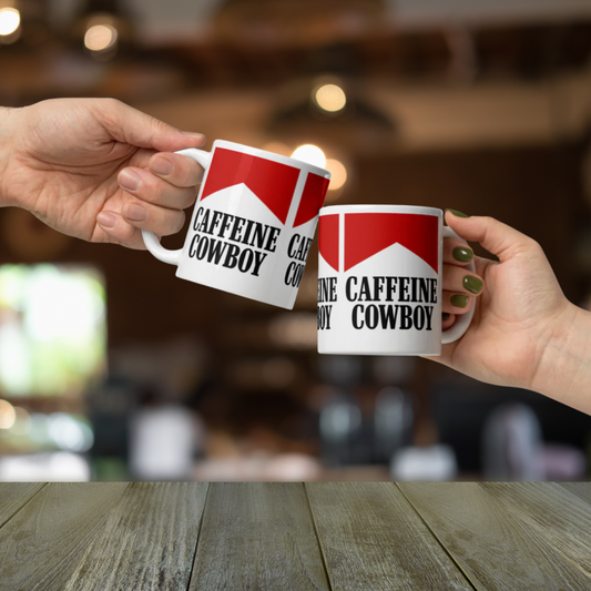 Two hands holding mugs labeled 'Caffeine Cowboy' against a blurred cafe background.